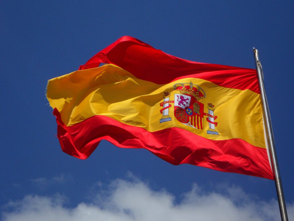 Spanische Flagge, leicht angerissen, vor blauem Himmel wehend.